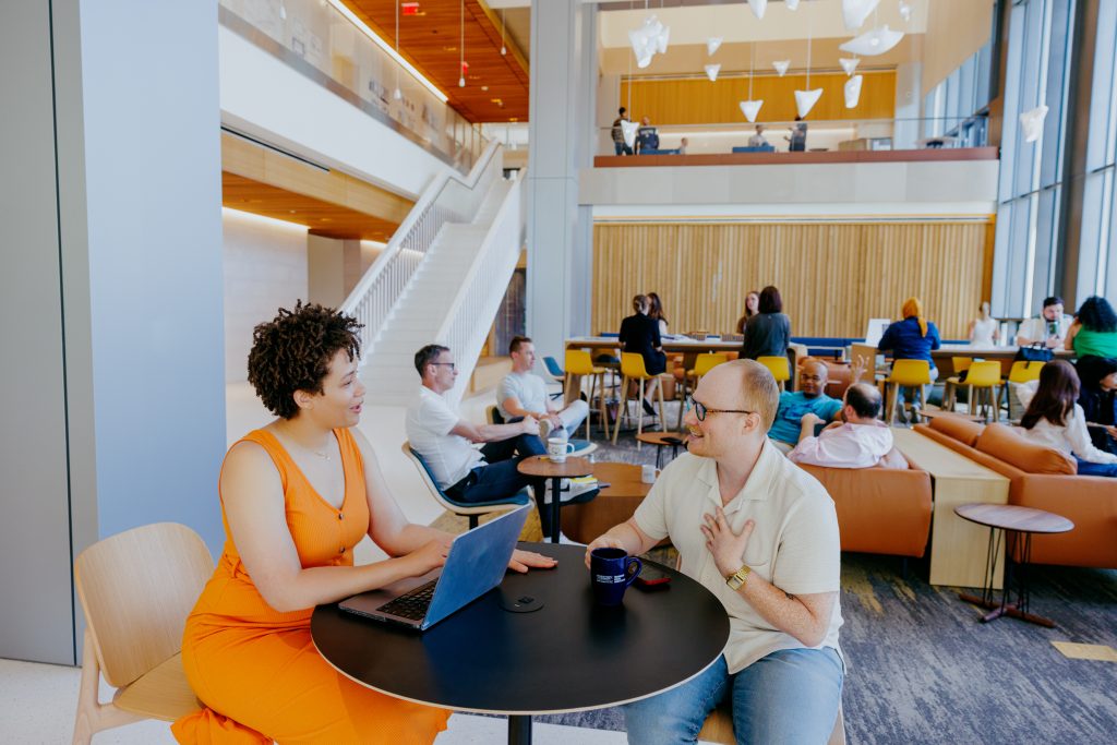 Two students sit at a small round table in an open atrium 