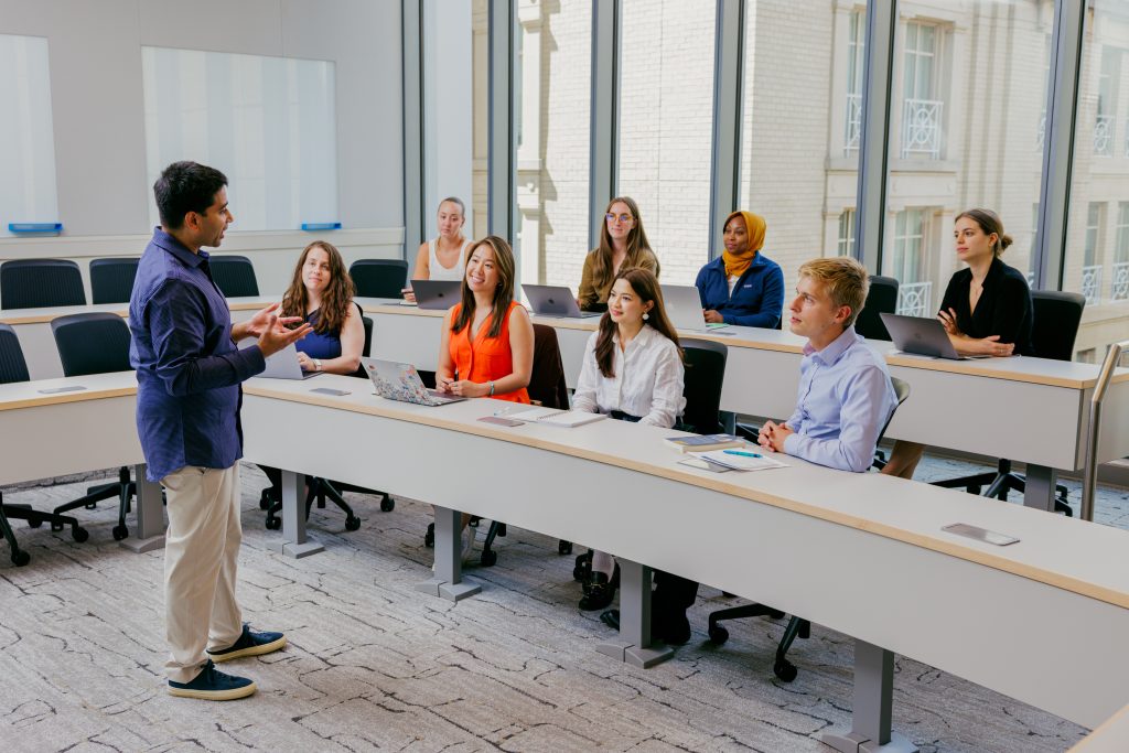 A group of students watching a professor teach in a classroom. 