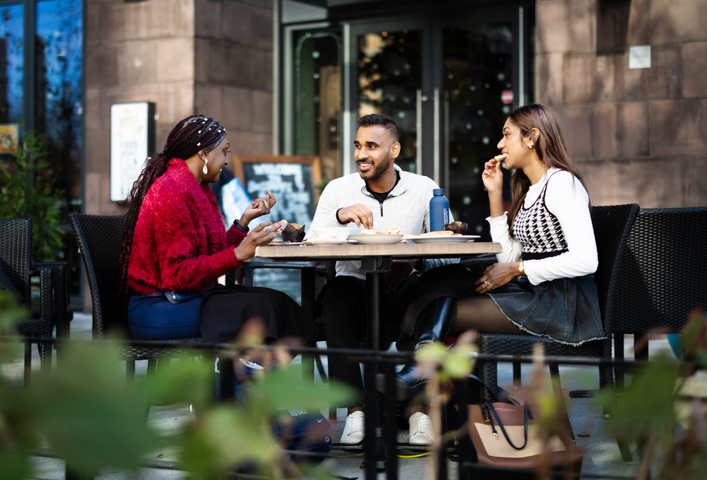 Two young women and a young man sit at a table while eating lunch