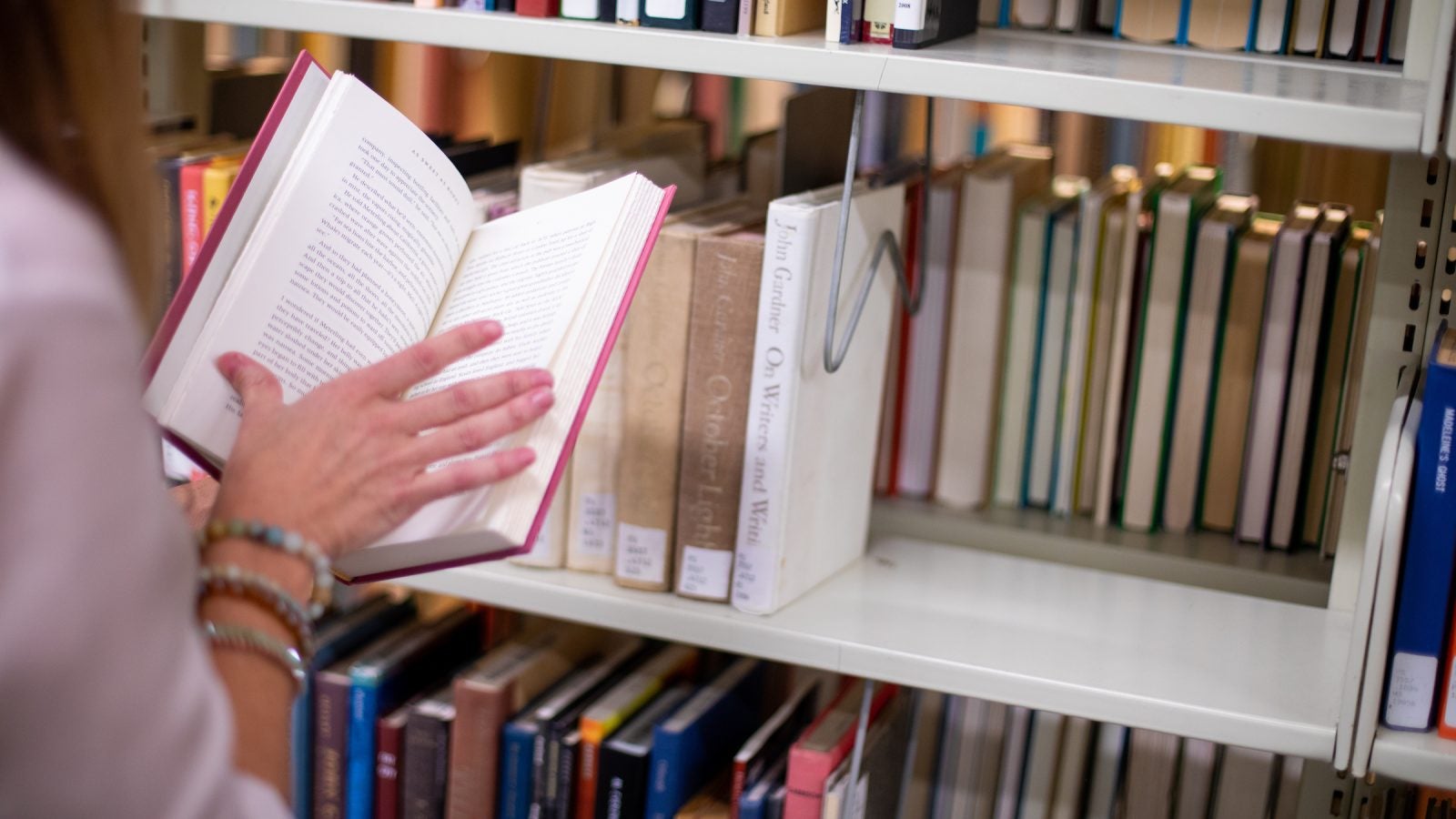 person opening a book in front of a library shelf