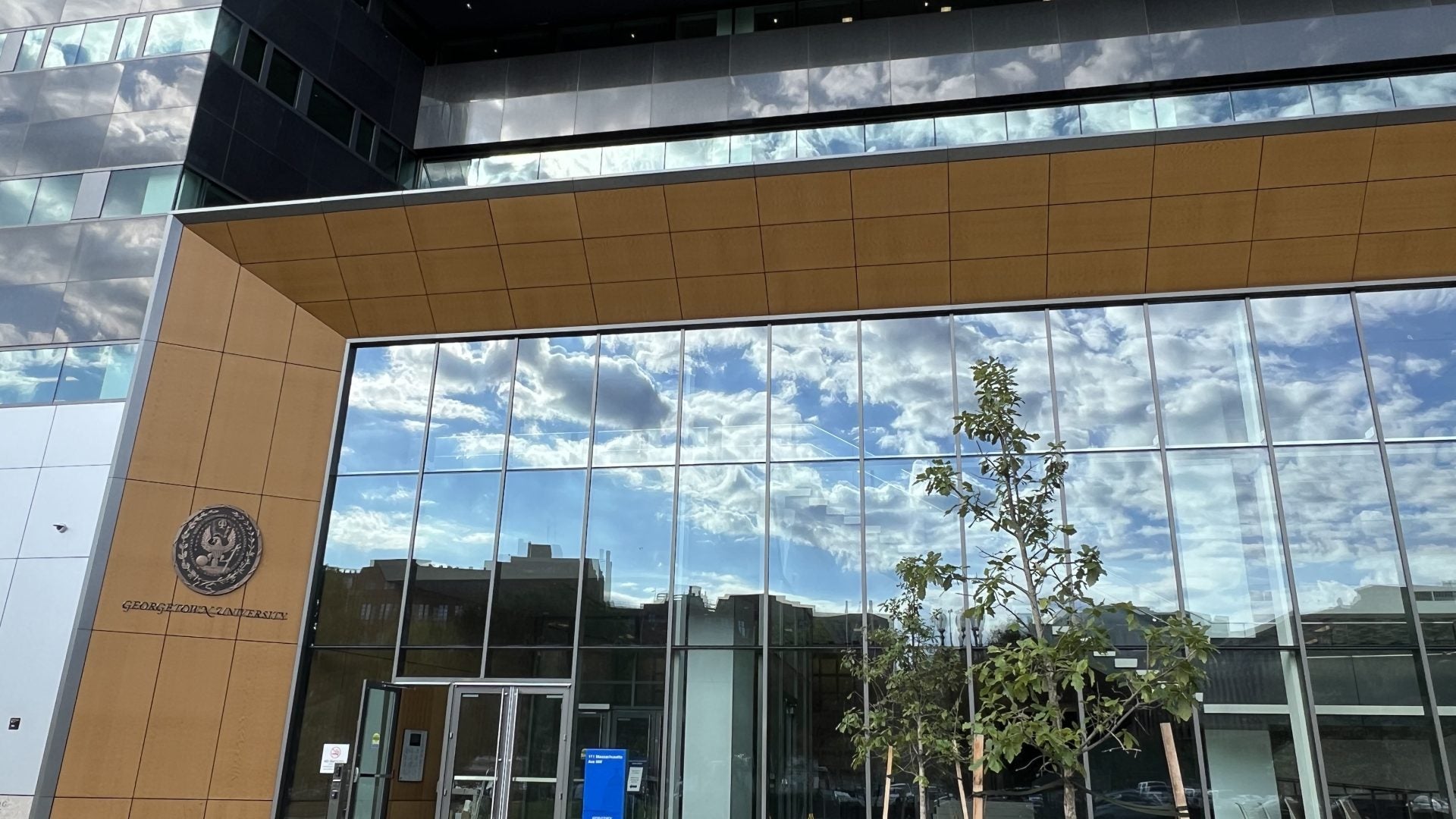 111 Mass exterior, with wood panels and highly reflective windows reflecting a cloudy sky