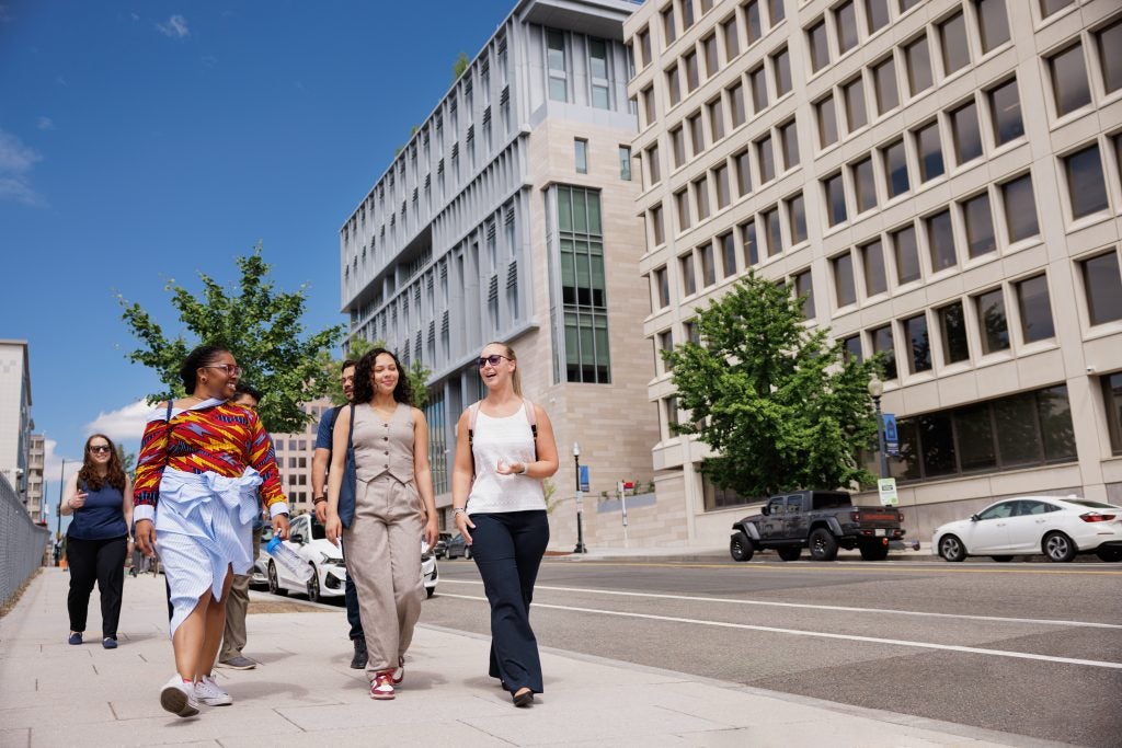 A group of students walking on the sidewalk through downtown DC on a sunny day.